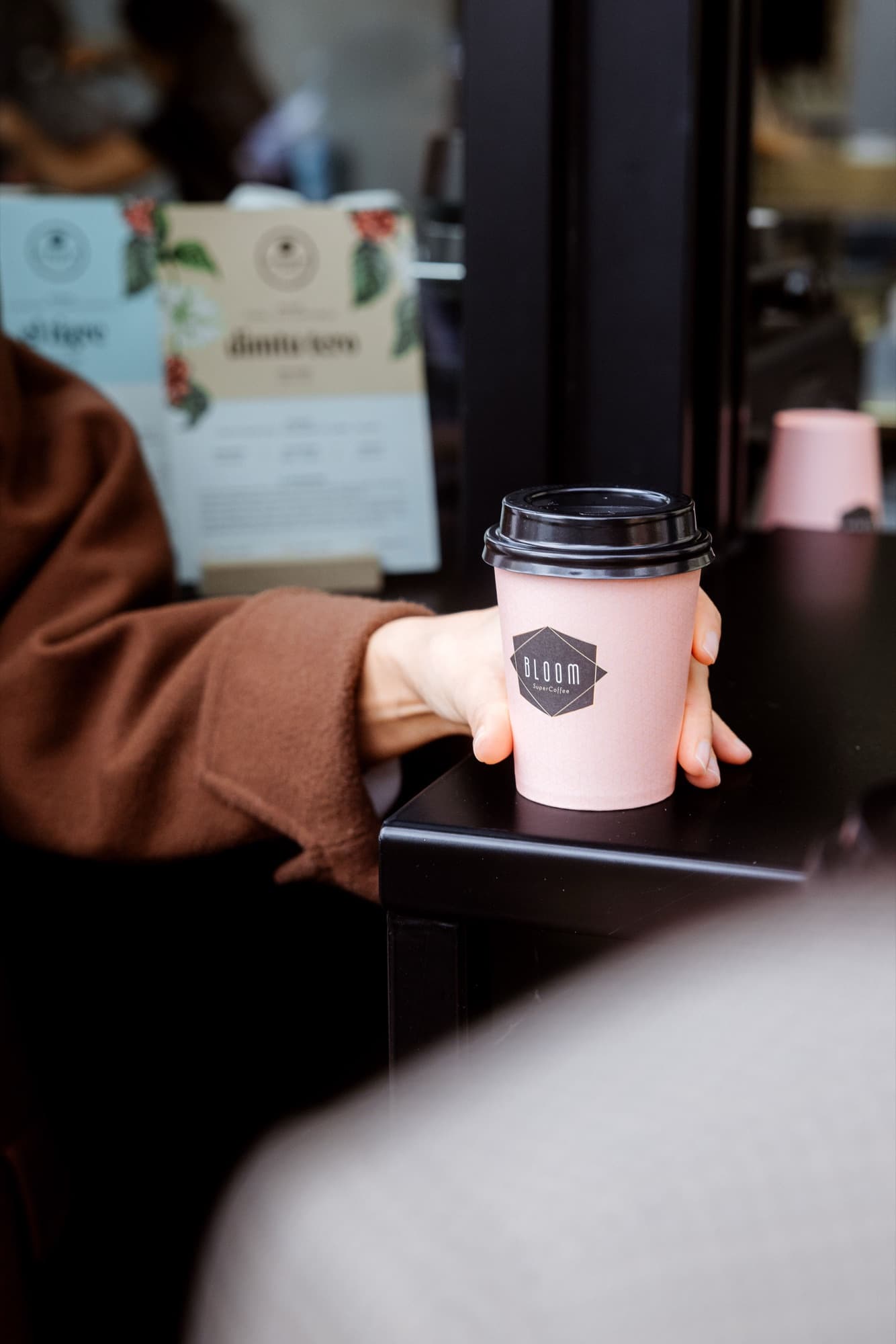 A hand holding a pink Bloom takeaway cup